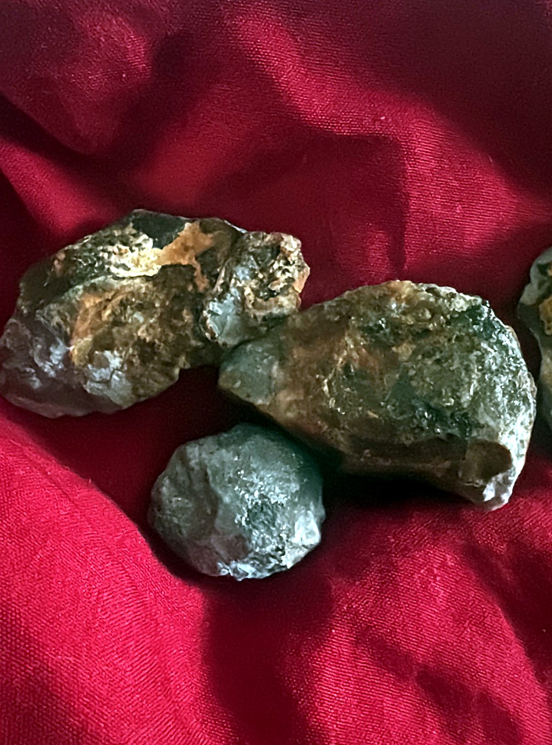 Three rough reddish-brown ruby corundum pebbles and one grey stone laid out on red cloth for grading