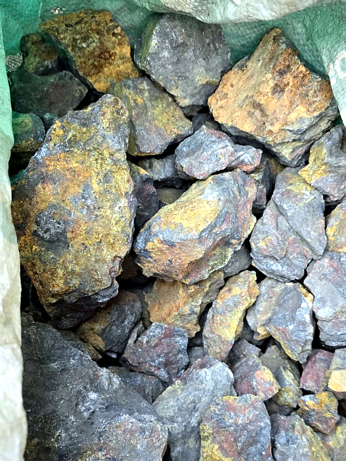 Bulk sack of hand-sorted ore chunks showing grey sulphide and yellow-brown oxidised surfaces