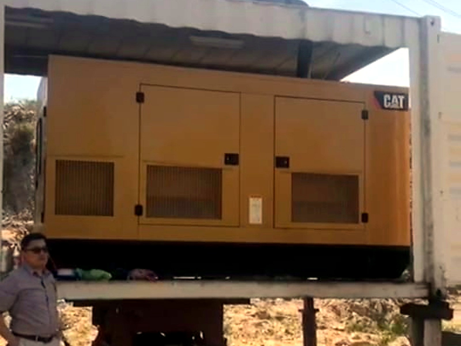Large yellow CAT generator installed inside an open-sided white shipping container at a mine site