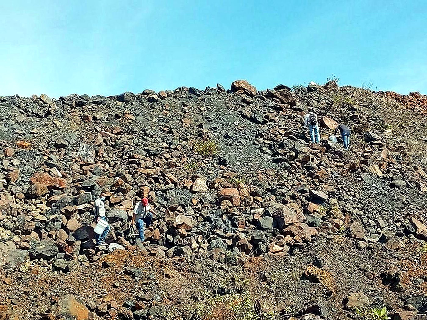 Several locally hired workers walking across a wide rocky quarry surface under a blue sky