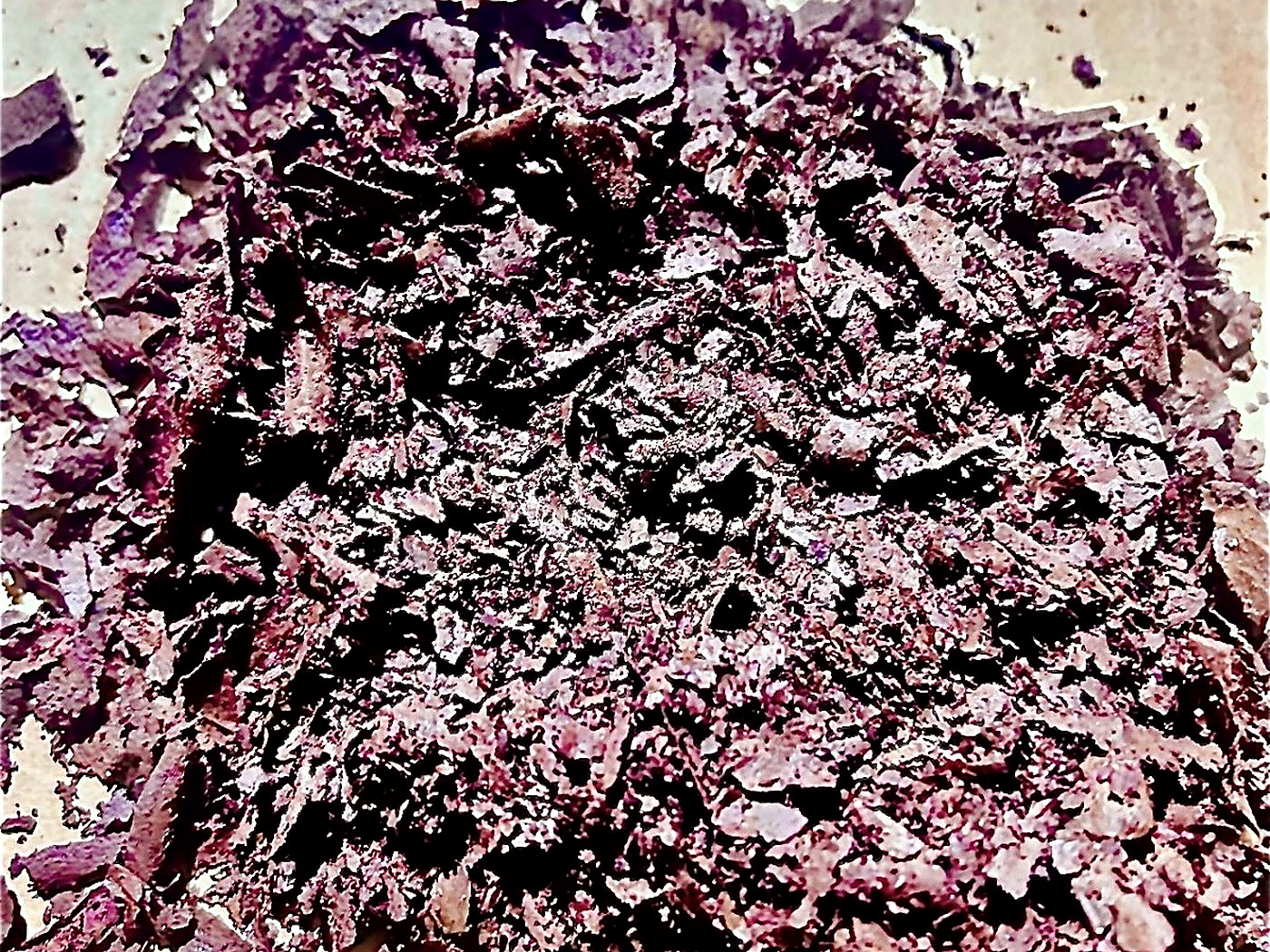 A mound of coarse purple-brown mineral flake concentrate spread on paper for particle size inspection