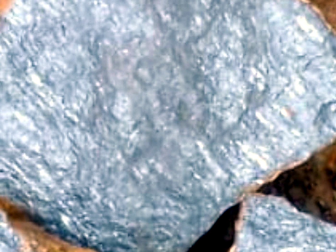 Extreme close-up of bladed silver-grey stibnite crystal faces on freshly split rock with rusty brown edges