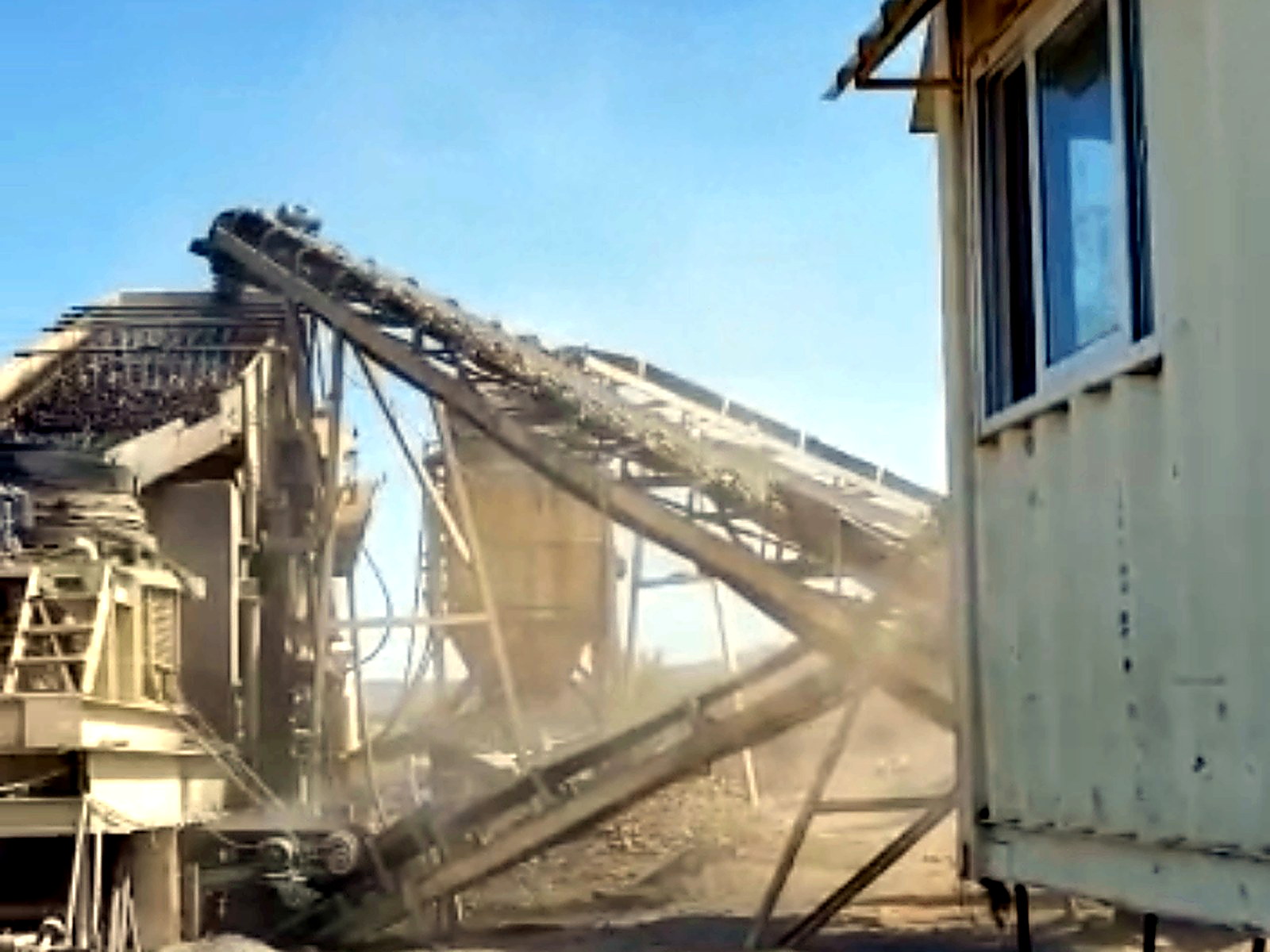 Mine processing yard with screening equipment, crossed conveyors, workshop tools and a white site office