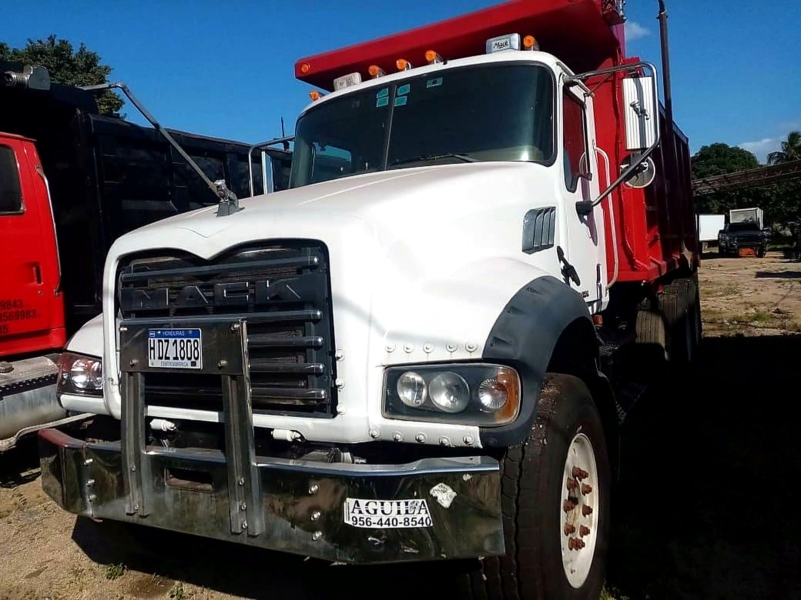 A white and red tipper haul truck parked on a dirt yard at a Central American mine site