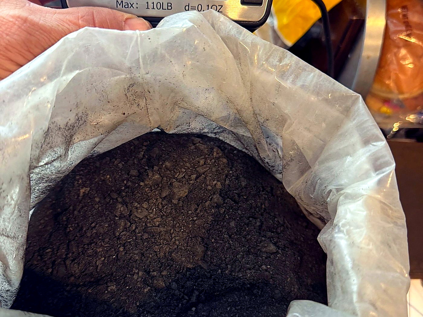 An open woven sack of dark mineral concentrate being weighed and logged at the site weigh station