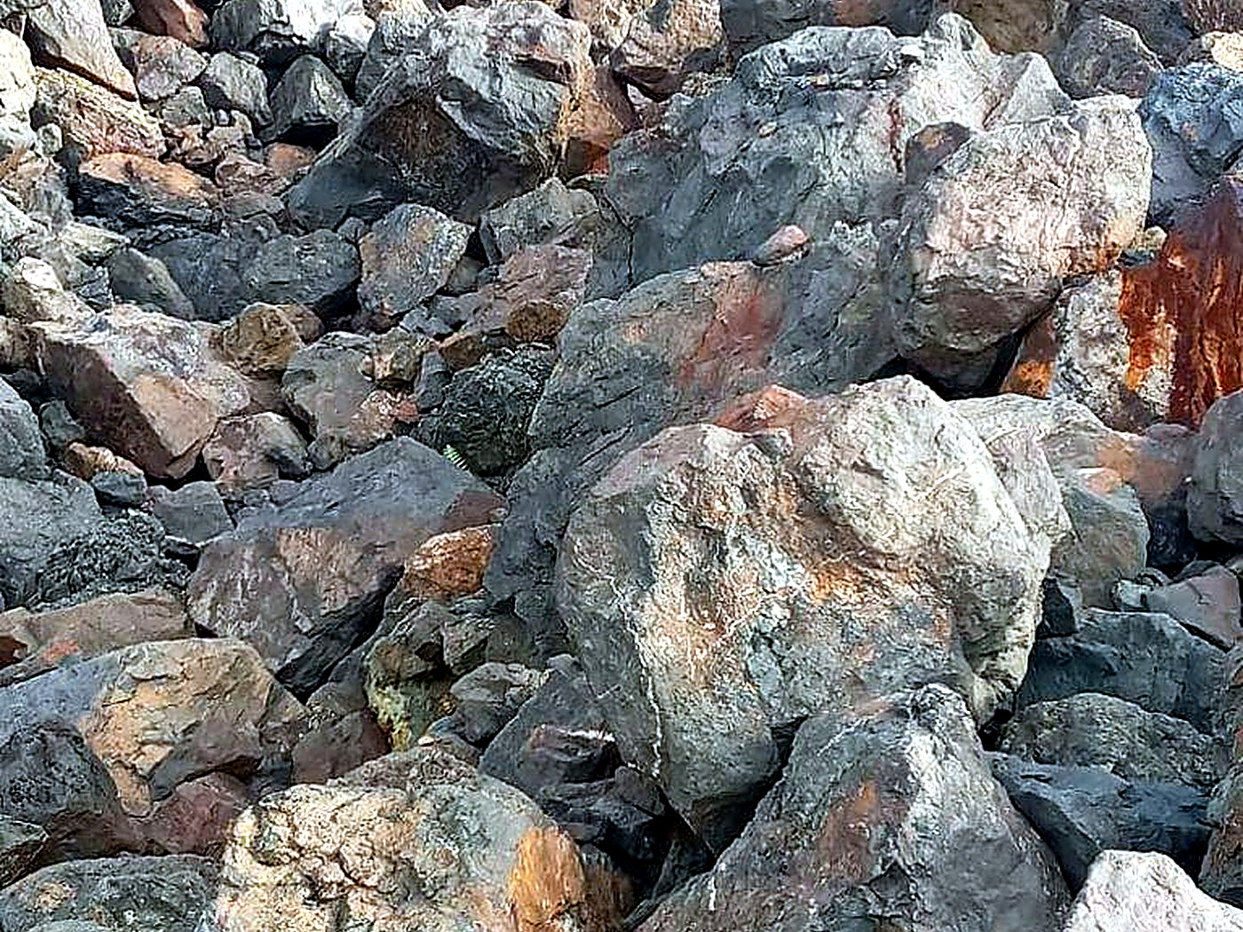 A freshly blasted pile of fragmented grey and rust-coloured rock on a mine working bench