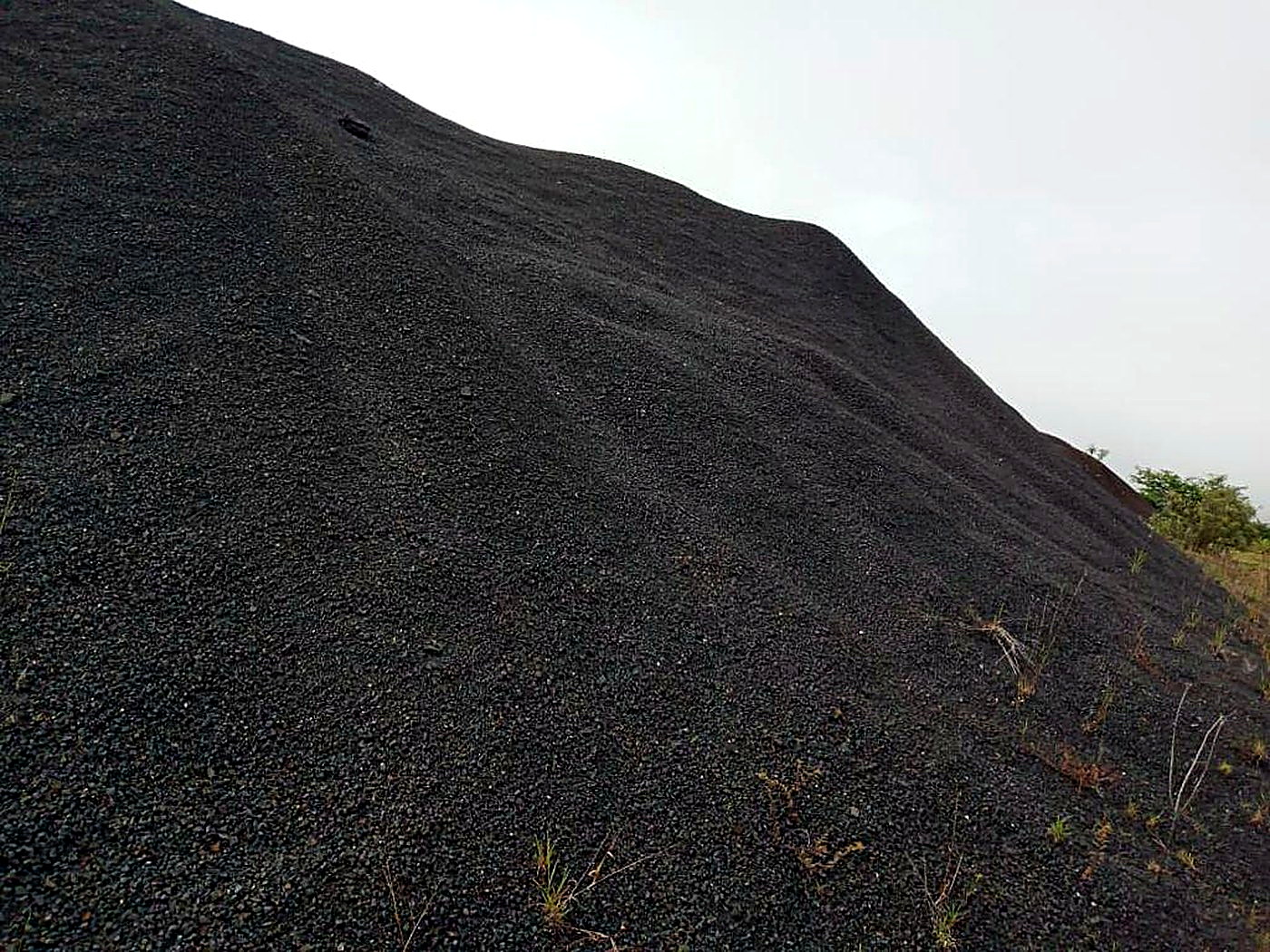 A large sloping stockpile of dark grey-black magnetite iron ore fines under an overcast sky