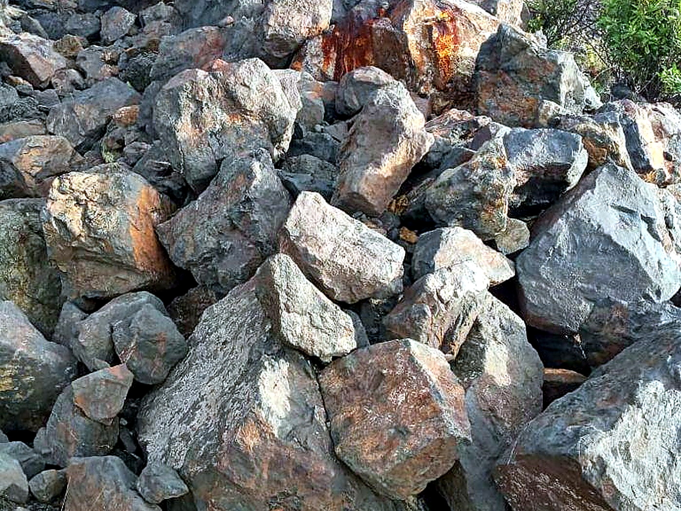 A stockpile of large iron-stained grey and rust-coloured ore boulders on a mine bench