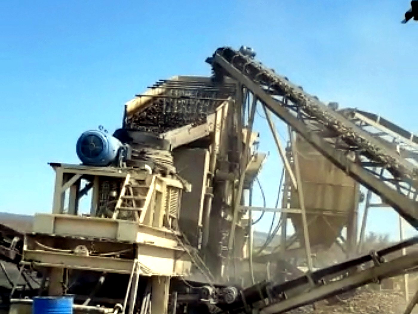 A mobile cone crushing and screening plant with conveyors running under a clear blue sky at a mine site