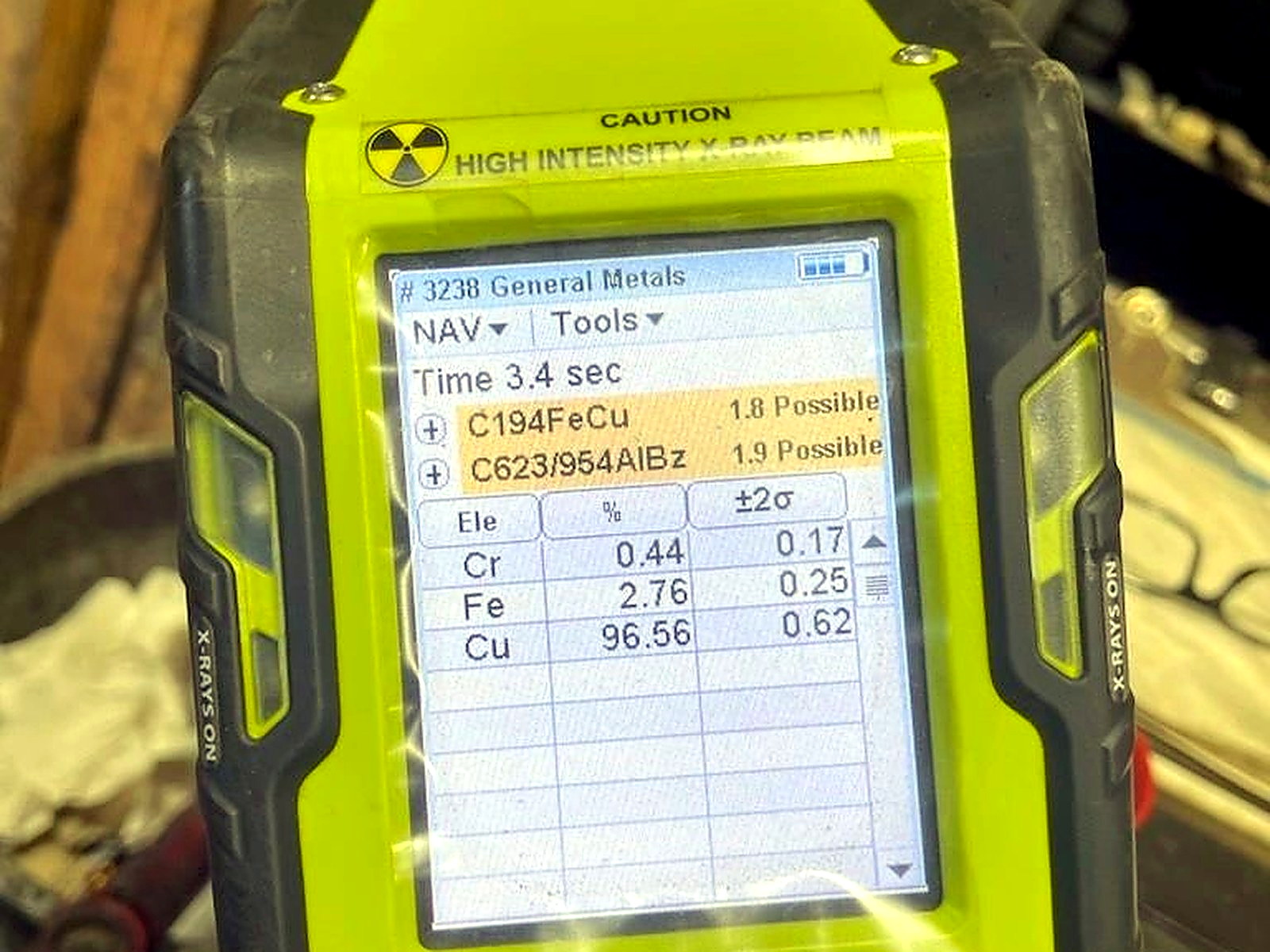 A yellow handheld XRF analyser screen showing a copper reading of 96.56 percent with iron and chromium values