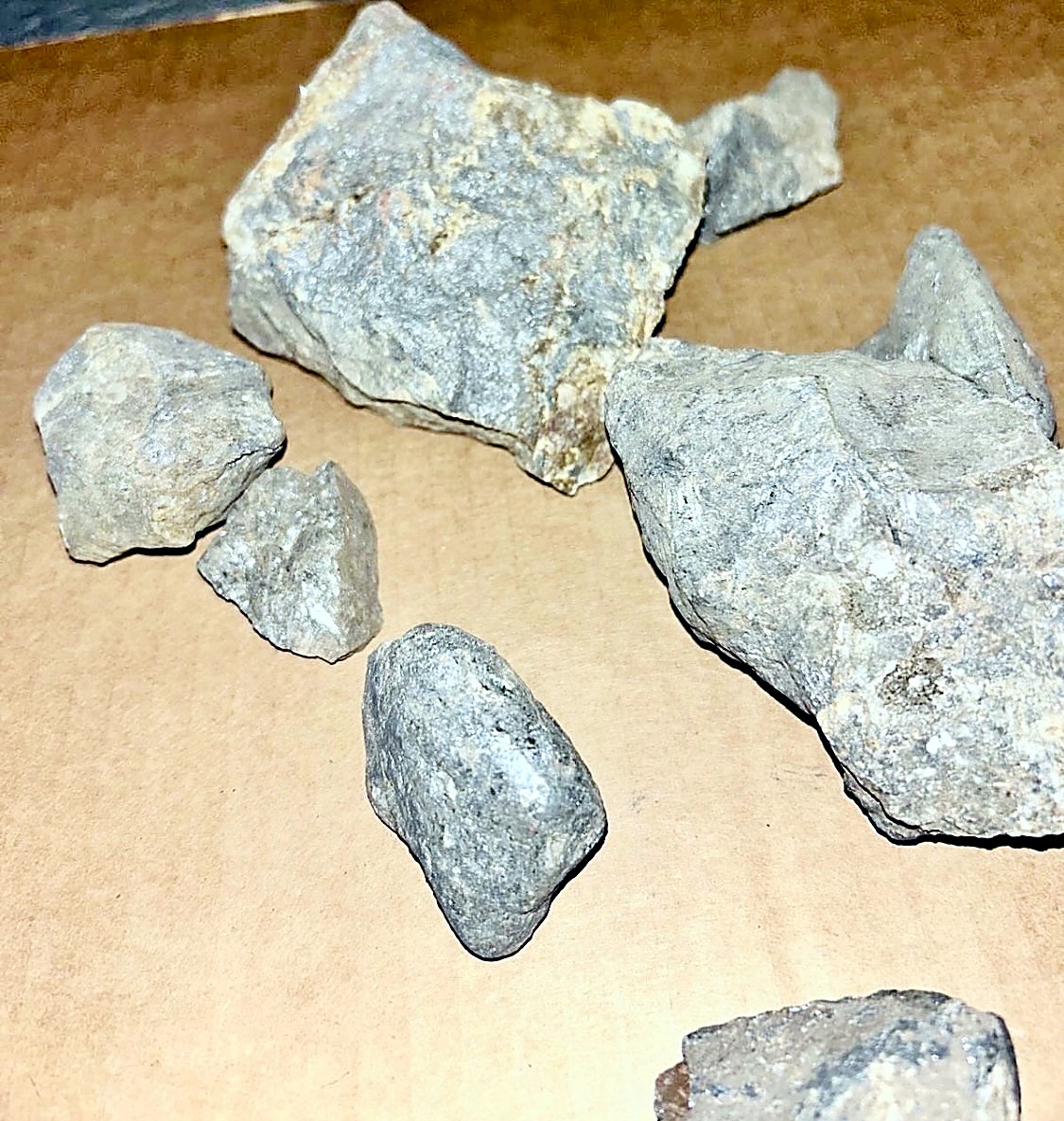 Several grey antimony ore rock fragments of varying size arranged on a tan paper surface for sampling