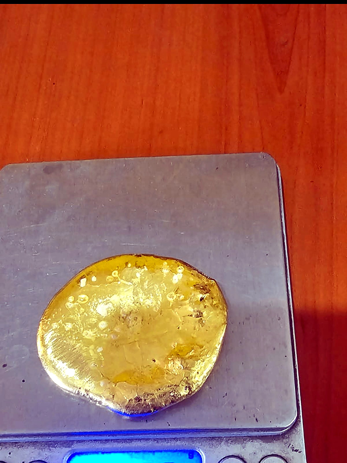 Round yellow gold button weighing 238.4 grams on a digital laboratory scale