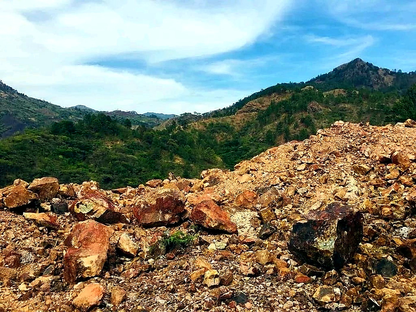 A large stockpile of reddish-brown run-of-mine iron ore rock beneath a cloudy sky