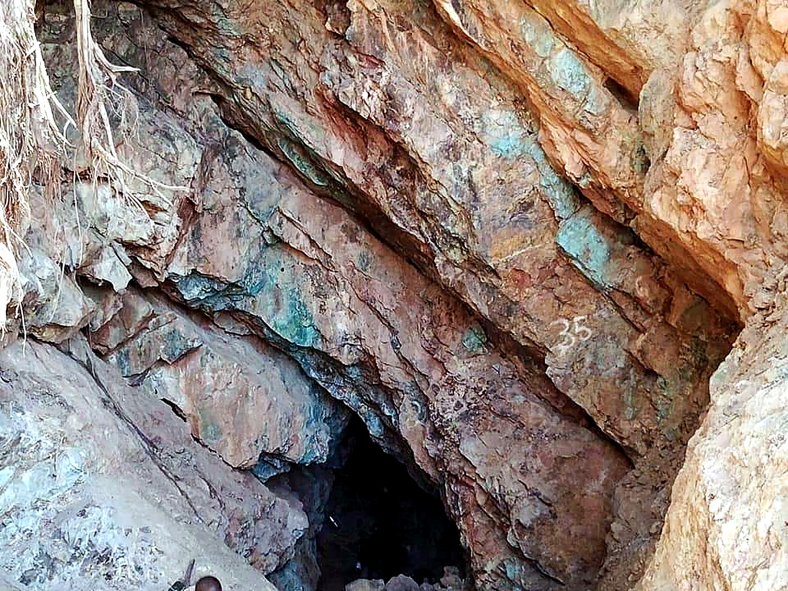 A dark underground adit portal cut into rock covered in turquoise copper oxidation staining