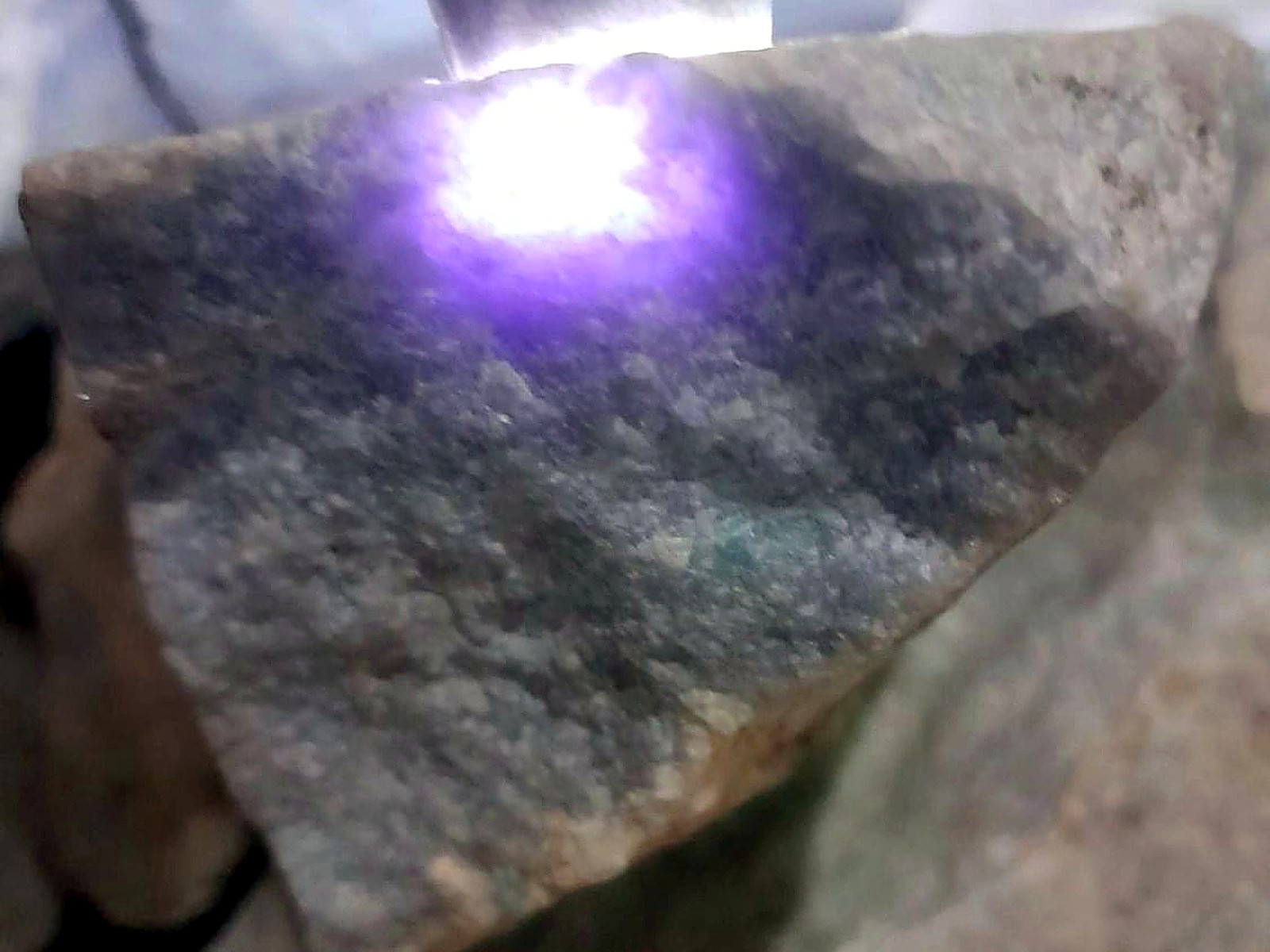 A bright violet laser spot burning a test point on a grey rock sample during spectrometry analysis