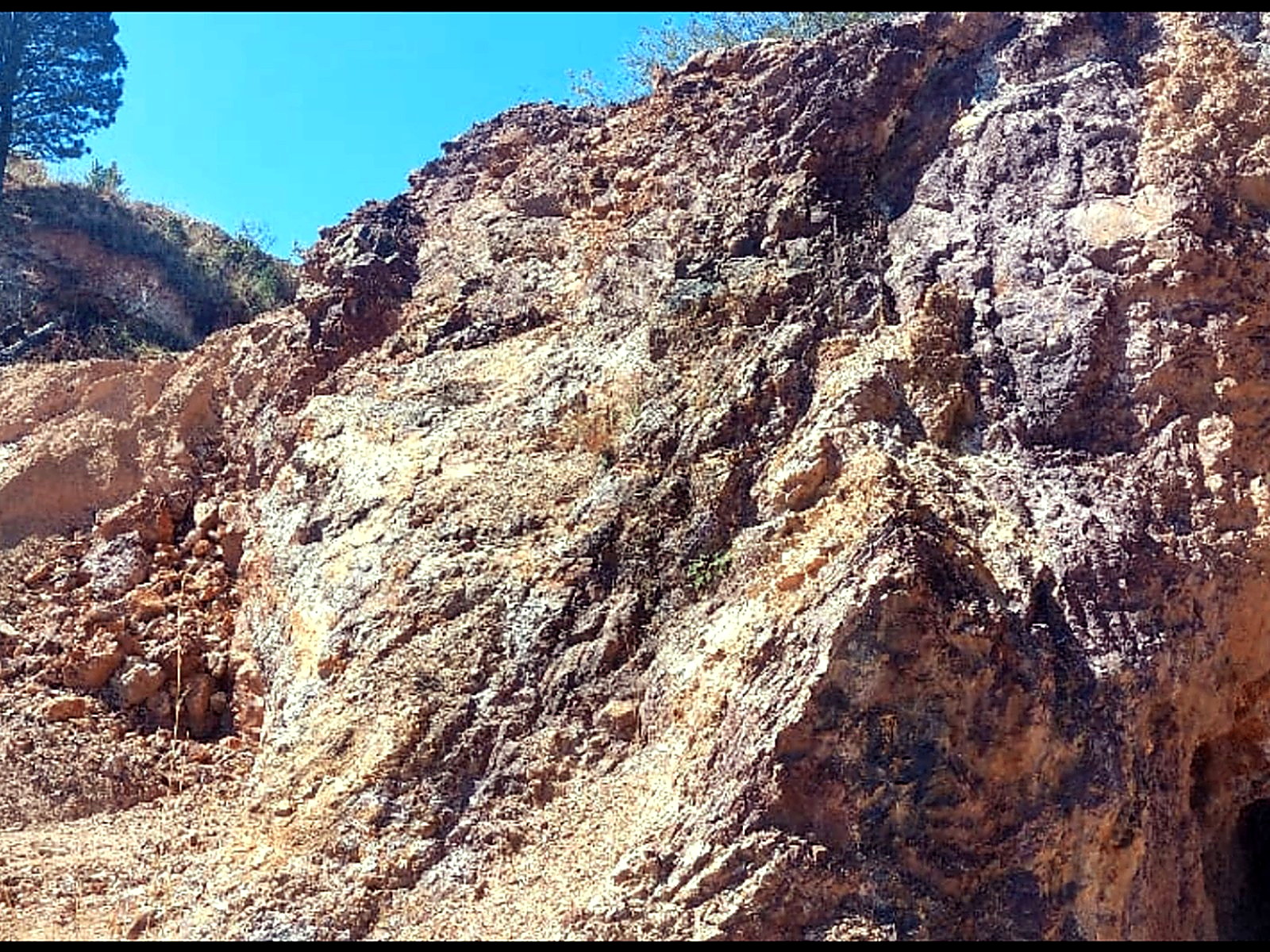 Steep tan and orange rock face on a hillside with a dark tunnel entrance at its base
