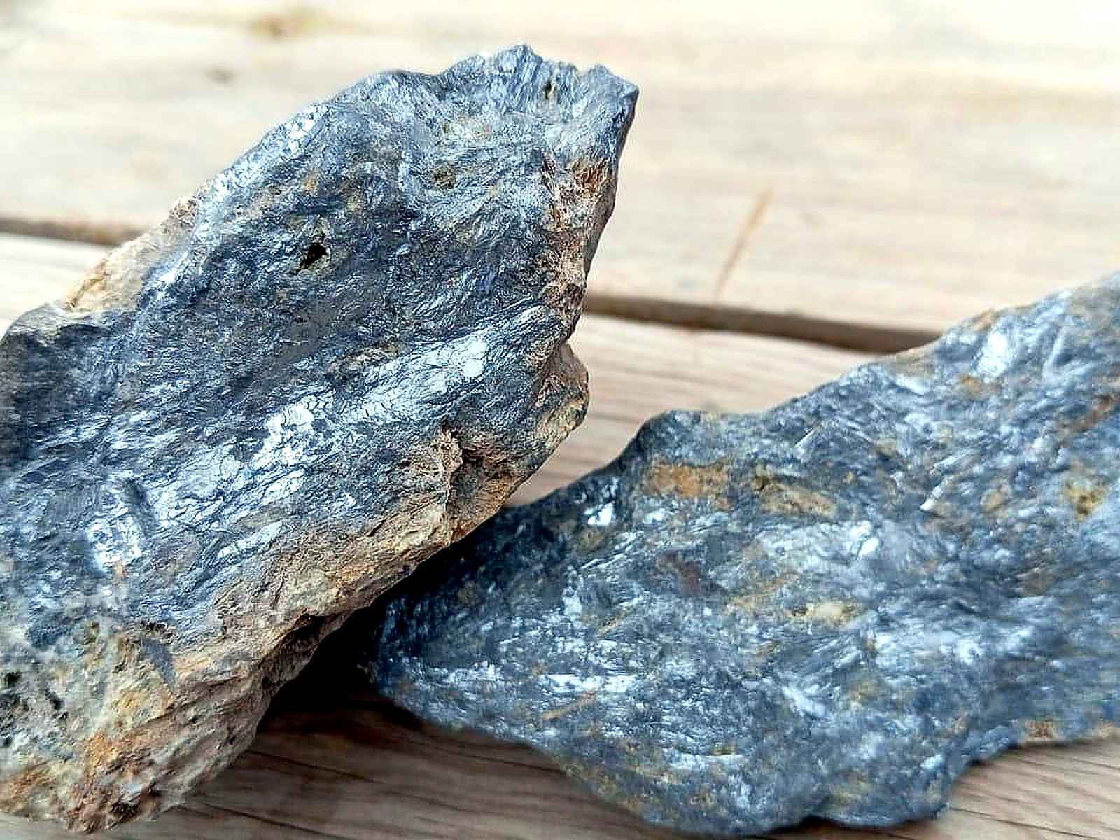 Two metallic silver-grey mineral specimens with bladed crystal texture resting on weathered timber boards