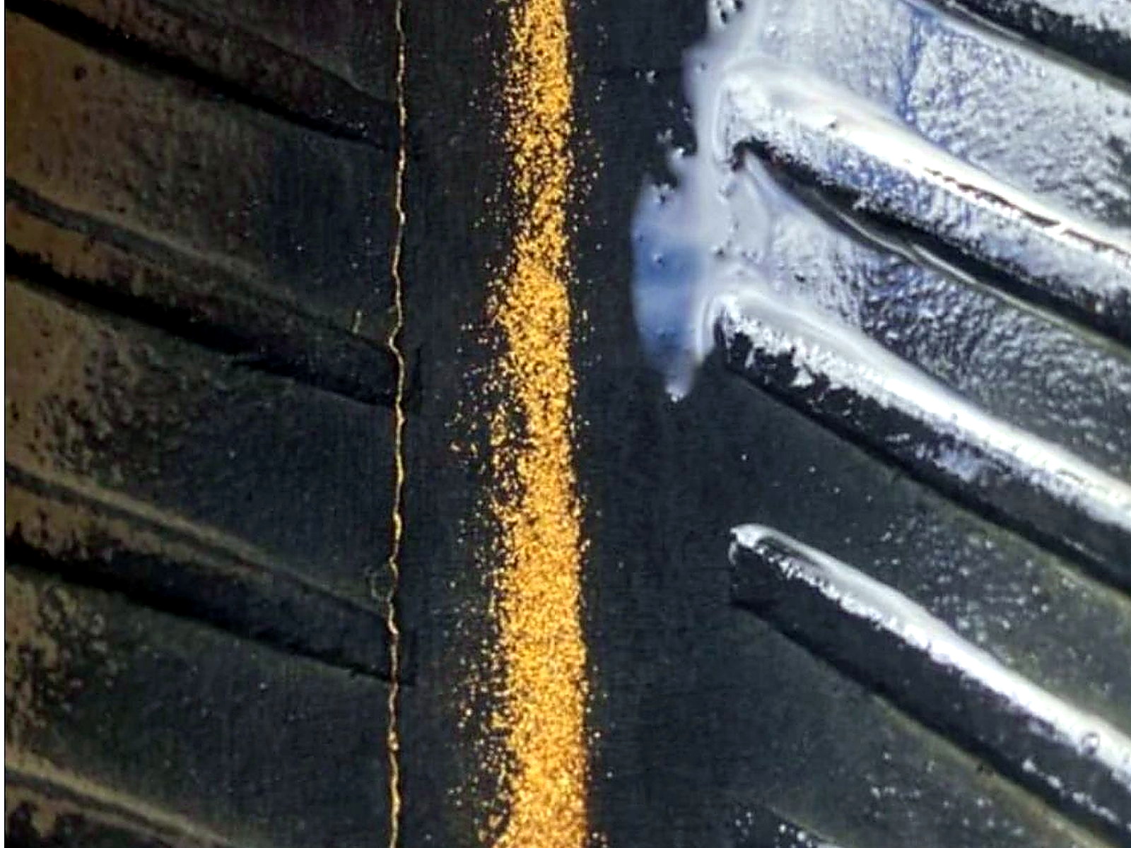 A line of bright yellow gold particles trapped along the black rubber riffles of a wash plant sluice mat