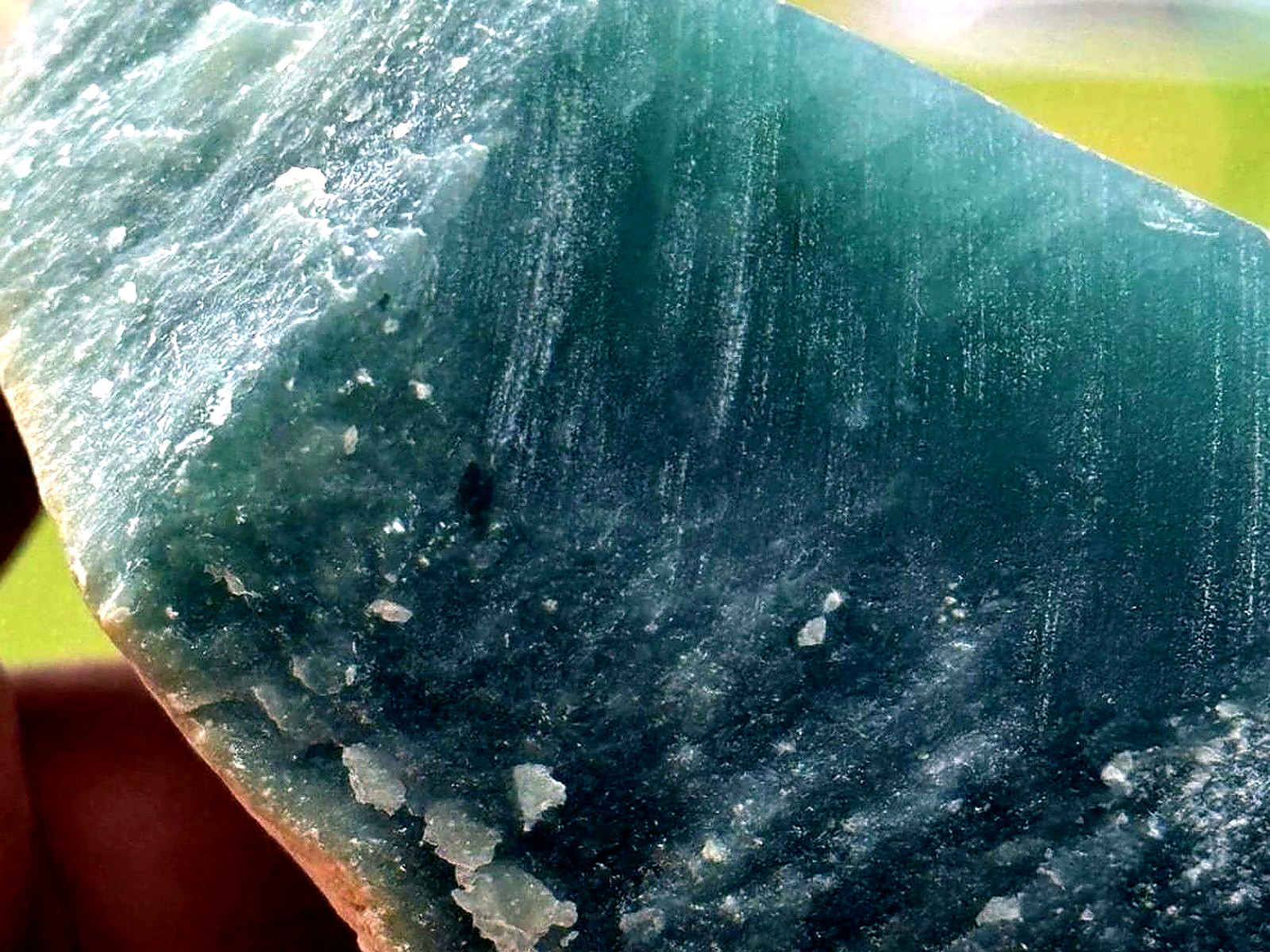 A hand holding a large block of blue-green jade rough with a fine banded texture