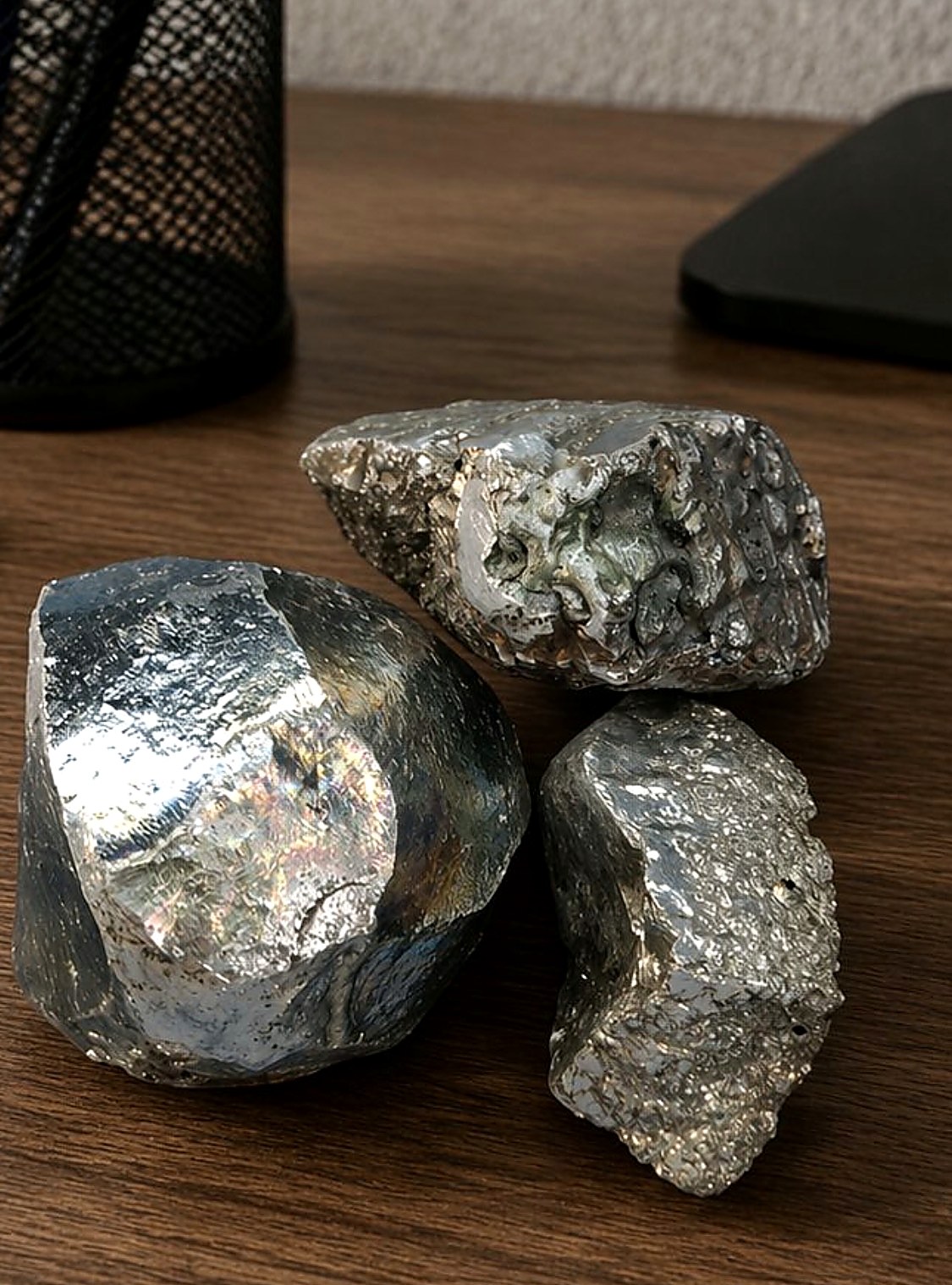 Three bright silvery metallic platinum and nickel bearing mineral specimens on a wooden desk