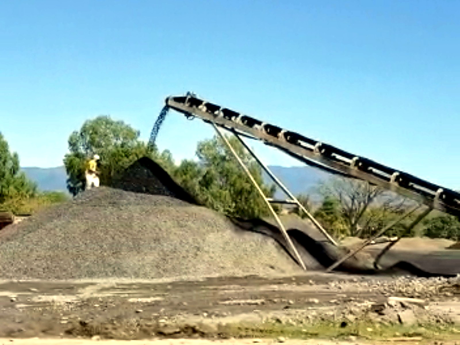 Inclined conveyor discharging crushed grey rock onto a conical outdoor stockpile