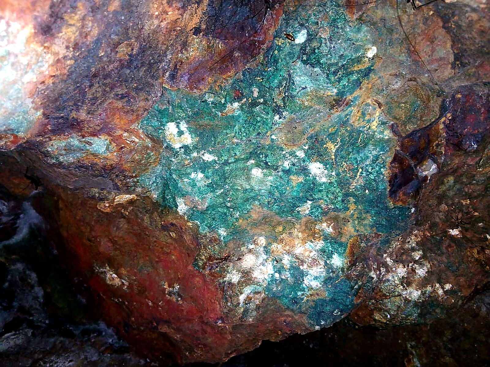 Rock face underground with a large patch of bright green copper carbonate staining surrounded by rust-red oxidised rock