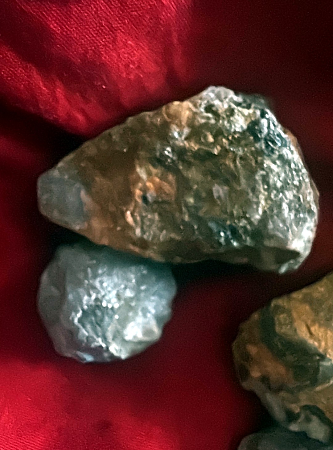Close-up of a rough ruby corundum stone with translucent red zones beside a smaller grey pebble on red cloth