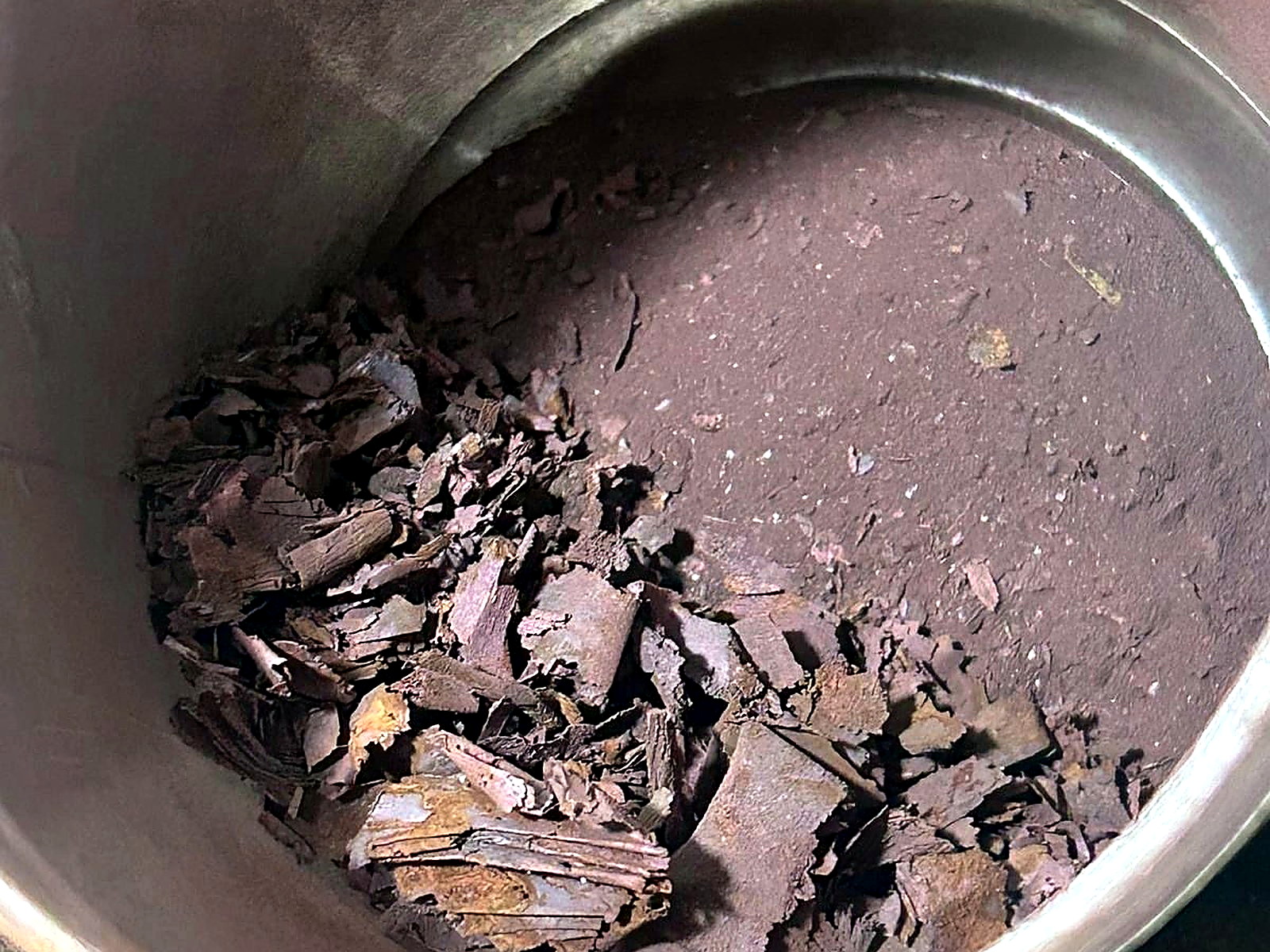 Dark purple-brown coarse mineral flake concentrate collected inside a steel drum