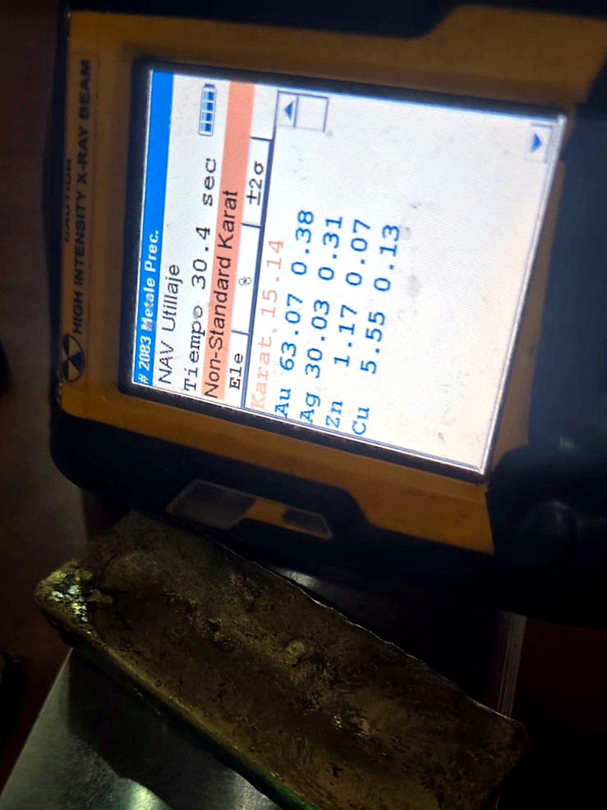 Rectangular gold-silver doré bar photographed beside an XRF analyser screen showing gold and silver percentages