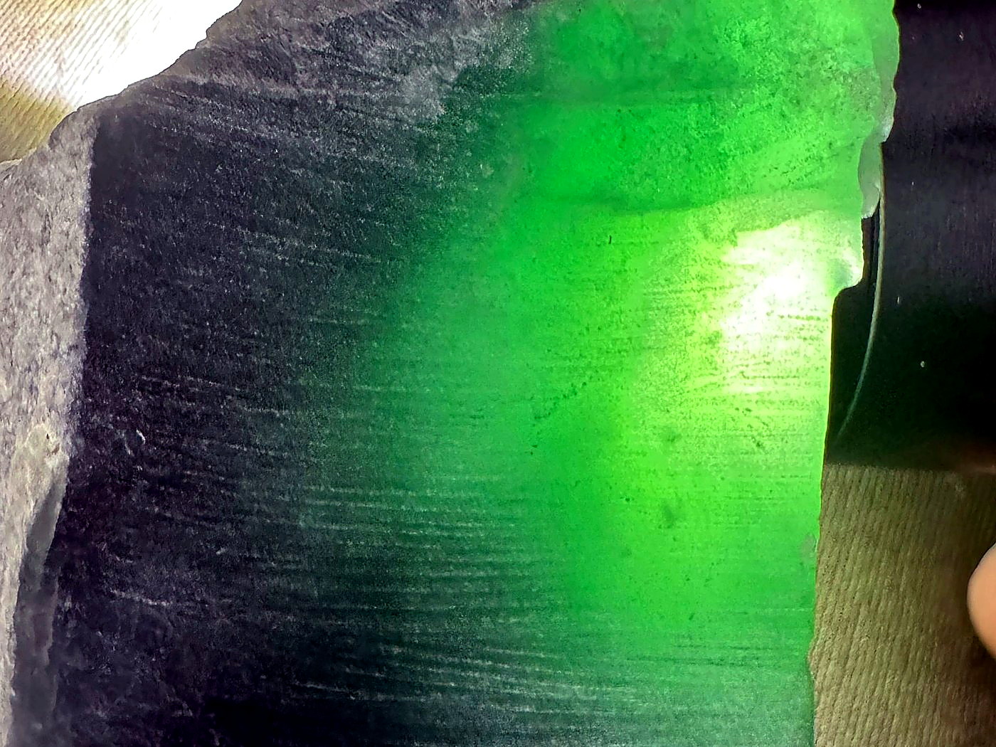 A cut jade slab glowing vivid green as a bright light is shone through it during translucency testing